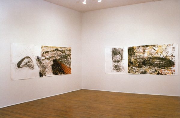 Two large ink drawings on paper, which feature expressive, distorted self-portraits of Mike Parr, alongside a mass of energetic black and brown ink lines and swirls. The drawings are mounted on the wall of a gallery.