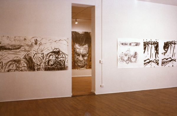 Large ink drawings on paper, which feature an expressive, distorted self-portrait of Mike Parr, alongside masses of energetic black and brown ink lines and swirls. The drawings are mounted on the wall of a gallery.