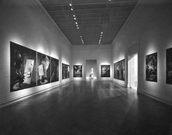 A series of large ink and charcoal drawings on paper, mounted on the walls of a long gallery. The drawings feature heavy architectural forms, black crows and lone human figures against dark backgrounds.