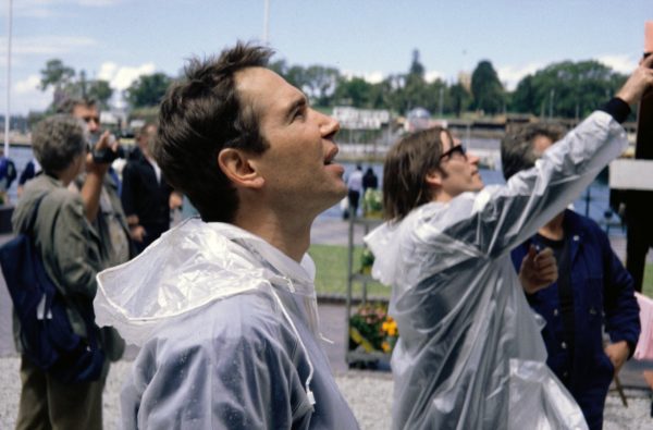 A man in a plastic raincoat looks upwards. A second man in a plastic raincoat points in the same direction.