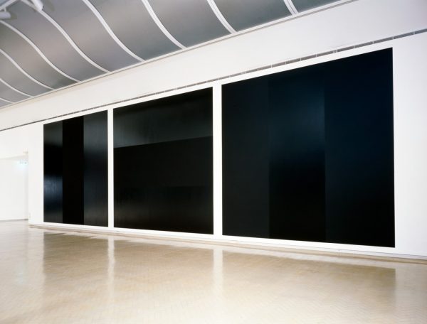 A series of three paintings, featuring geometric arrangements of bands in matt and gloss black, mounted on a gallery wall.