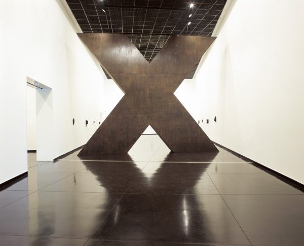 A heavy, bronze-coloured X stretches from the floor to the ceiling, and across the width of a contemporary art gallery.