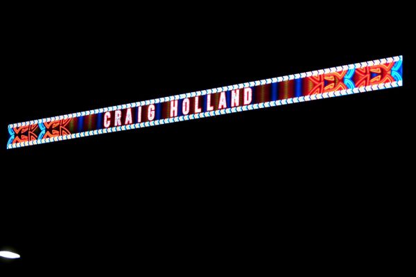 The name Craig Holland, written in bright lights, with a bright red and blue geometric pattern, against a dark night sky.