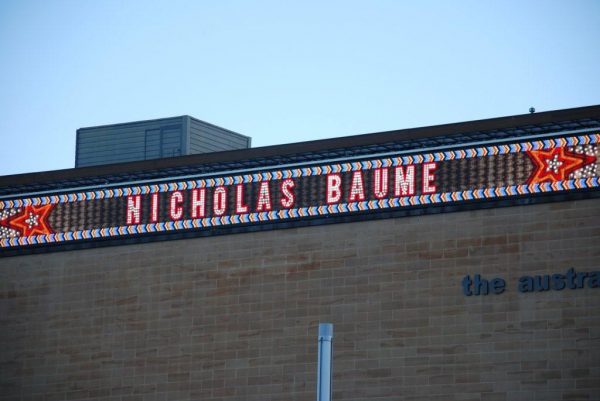 The name Nicholas Baume, written in bright lights, with a pattern of red and yellow stars, across the front wall of a museum.