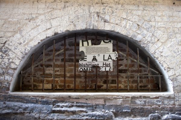 A large white puzzle piece, showing the fragment of a street map, hangs on a metal grate inside the niche of an old brick wall.