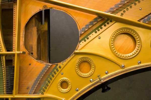 A round hole cut into the centre of a grand piano, with the piano strings and hammers removed around the hole.