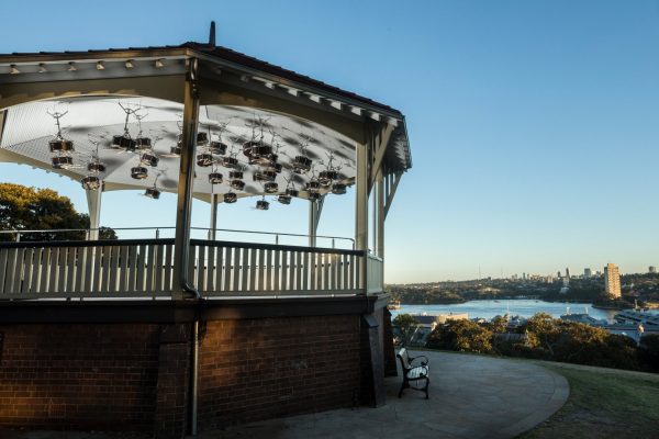An arrangement of 38 snare drums, hung upside down from the ceiling of an old rotunda, in a tree-lined park, on a hill, overlooking a wide harbour.