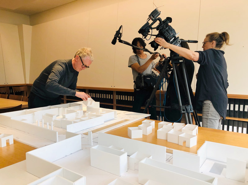 Michael Landy adjusts a cardboard exhibition model, while being recorded by a film crew.