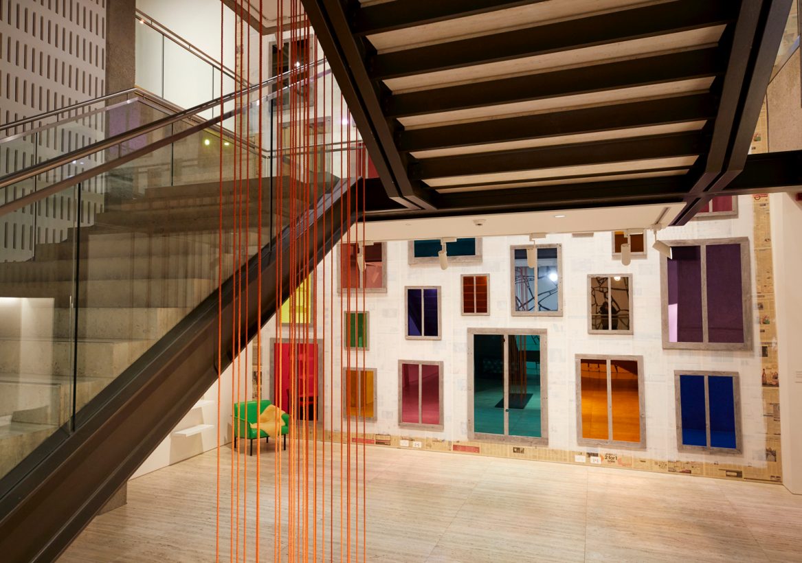 Around 20 long strands of dark orange rope, suspended vertically through the middle of a staircase in an art gallery.