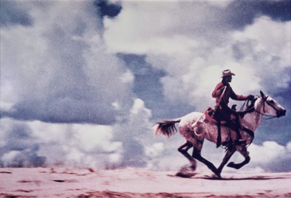 A cowboy rides a horse against a dramatic blue sky